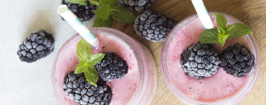 Pink smoothies in two glasses with frozen blackberries and green mint leaves on the top