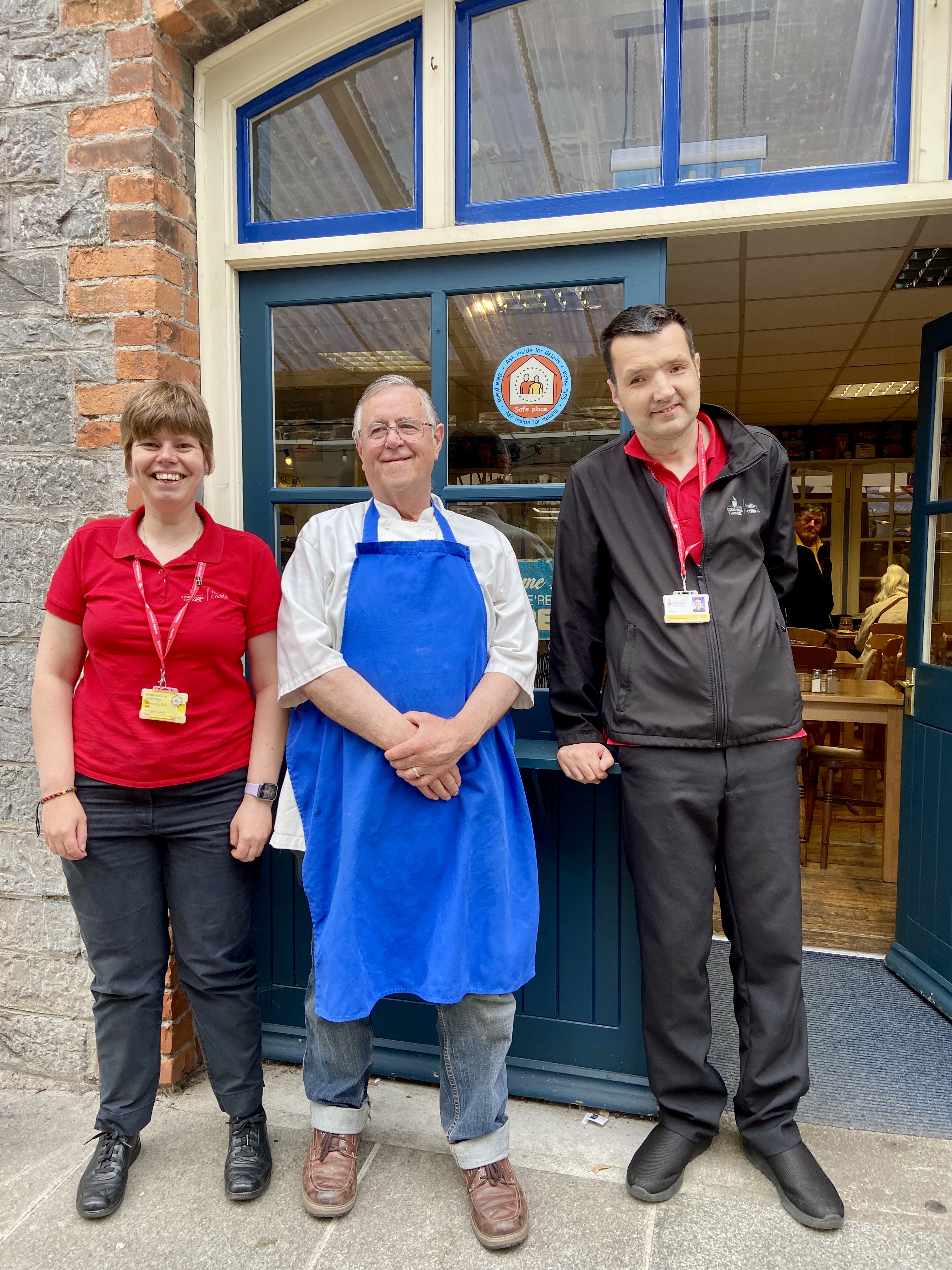 image of 2 of the CHAMPs team stood with a member of staff at Fodders Truro with a safe places sticker in the window