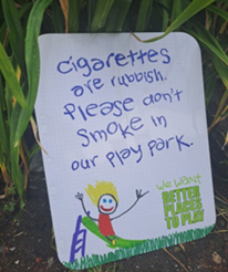 image of a sign that reads "cigarettes are rubbish, please don't smoke in our playpark"