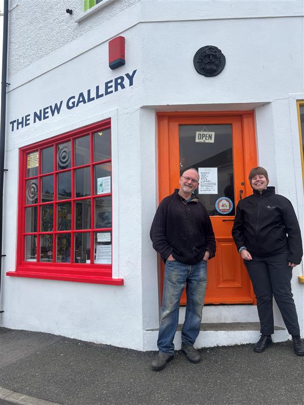 a member of the CHAMPs team stands with a member of staff from the new gallery New Gallery in Portscatho, showing the safe places sticker in their window